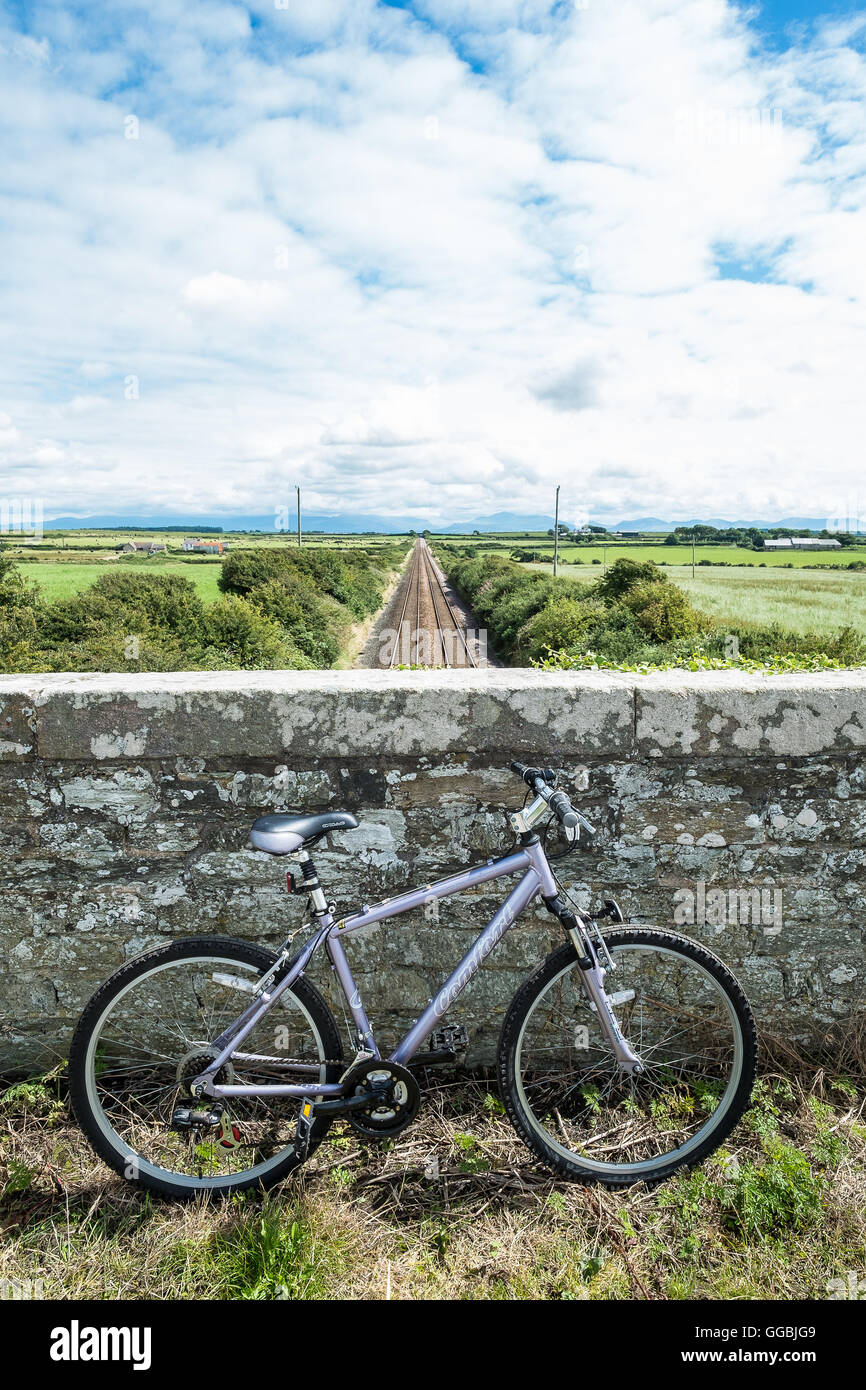 Bicicletta appoggiata contro la parete di un ponte che si affaccia su un treno via, Anglesey, Galles del Nord, Regno Unito, Mona mam Cymru Foto Stock