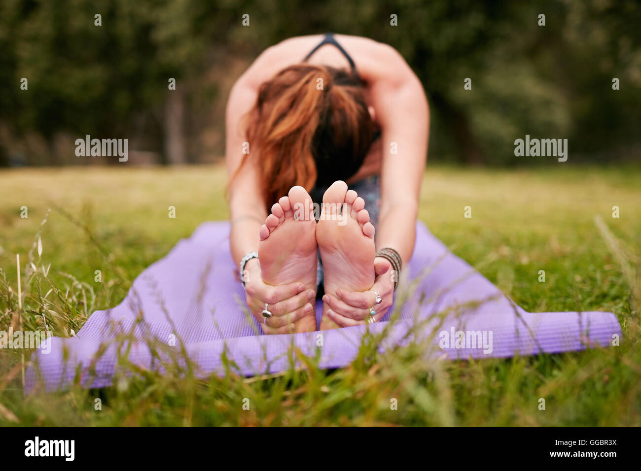 Giovane donna che fa yoga all'aperto su erba, pratica paschimottanasana posa. donna in forma seduta seduta in avanti piegata in posa durante il trai Foto Stock