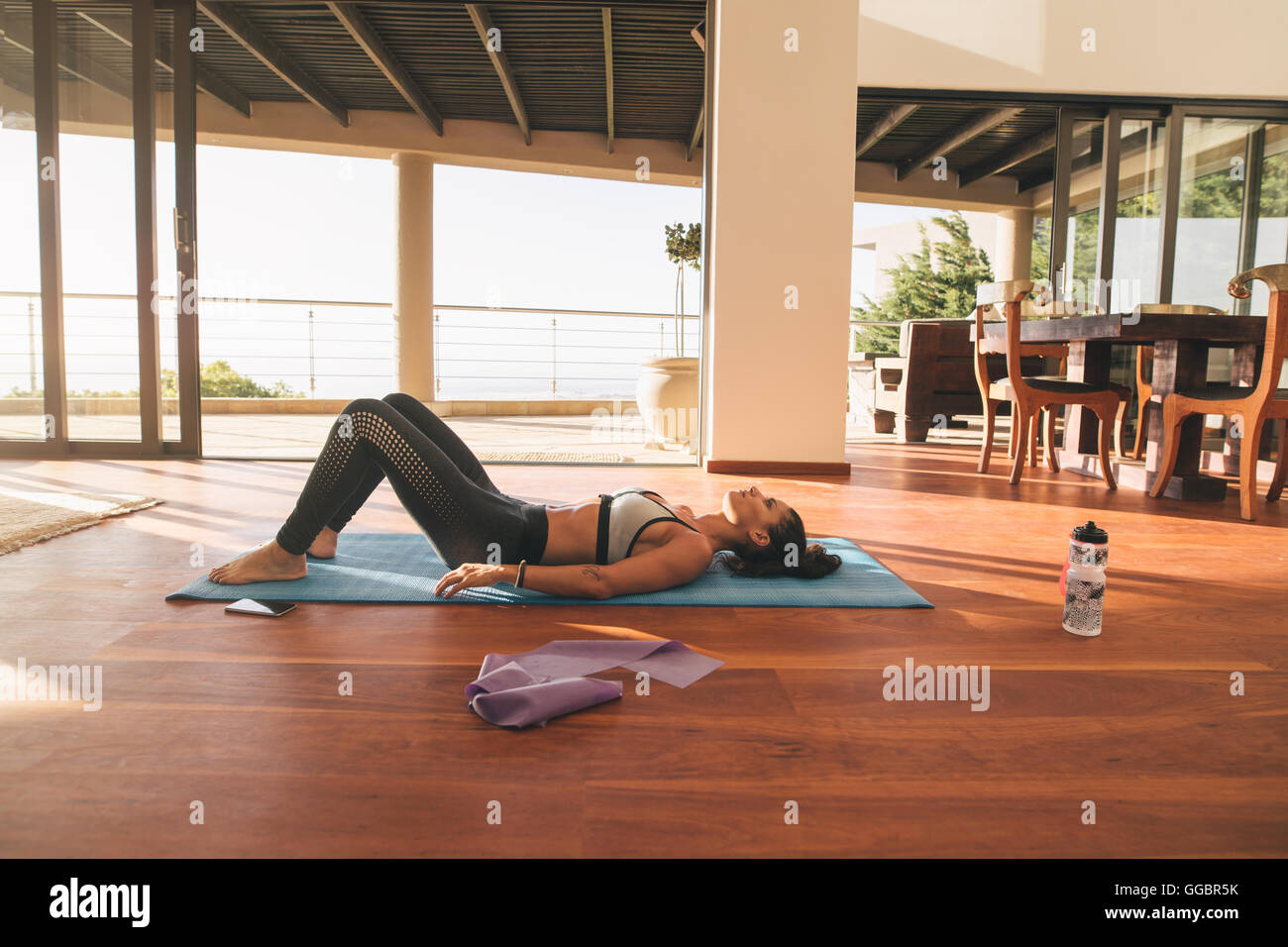 Colpo di donna fitness giacente sul tappeto di esercizio nel salotto del suo appartamento. Rilassante femmina sul pavimento dopo allenamento. Foto Stock