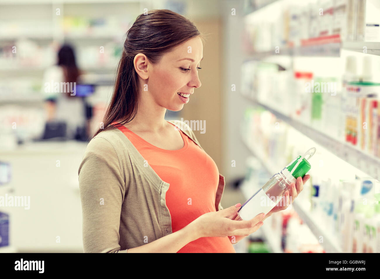 Felice donna incinta scegliendo lozione in farmacia Foto Stock