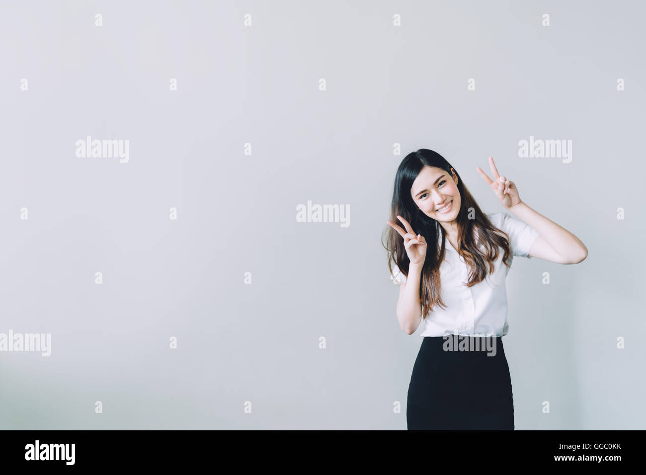 Carino università asiatiche ragazza facendo divertente posa di coniglio, copia dello spazio sul muro grigio sfondo Foto Stock