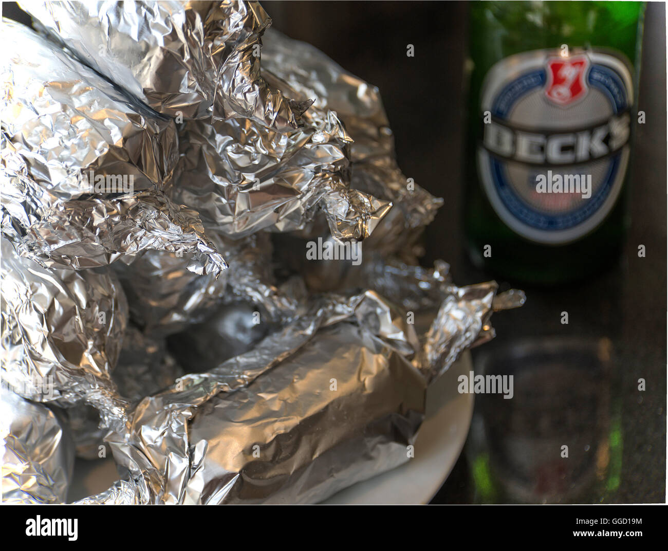 Granoturco appena grigliato sul COB avvolto in Tin Foil e una bottiglia di birra Becks su un tavolo da giardino a Shipton sotto Wychwood Oxfordshire Inghilterra UK Foto Stock