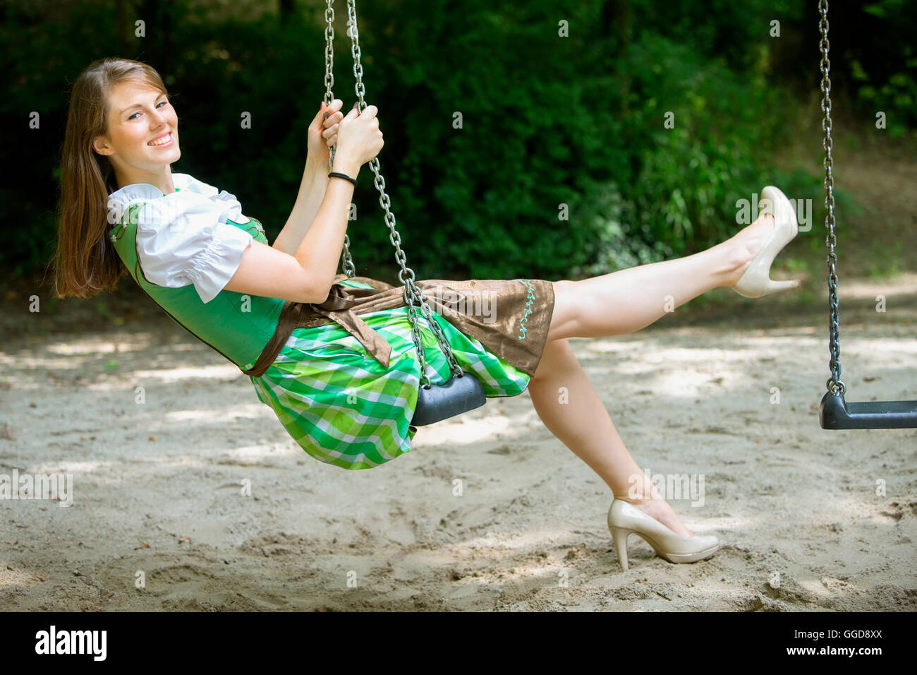 Donna bavarese in dirndl seduto su swing all'aperto Foto Stock