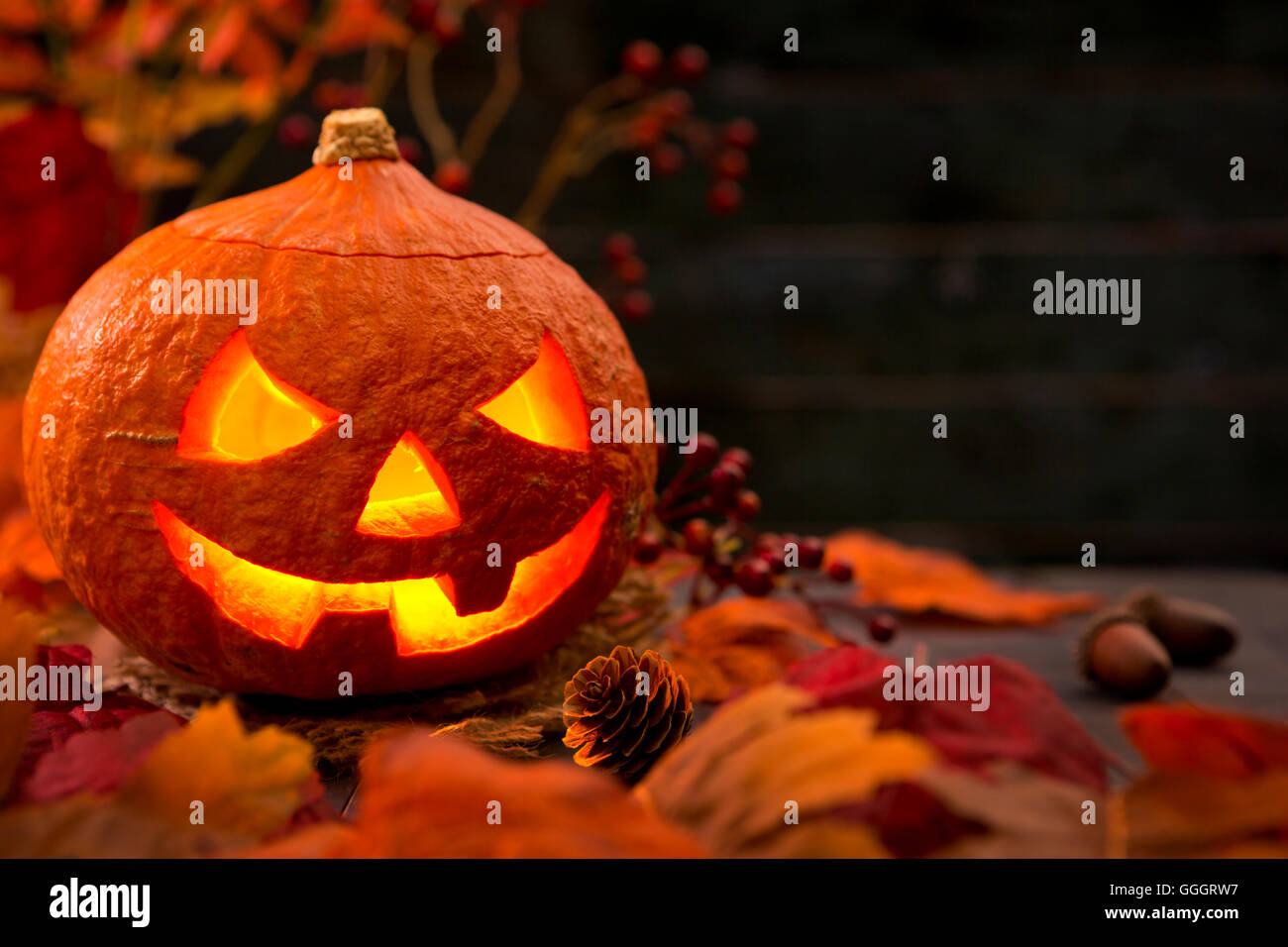 La masterizzazione di Jack O'Lanterna su un tavolo rustico con decorazioni d'autunno, oscuramente lit. Foto Stock