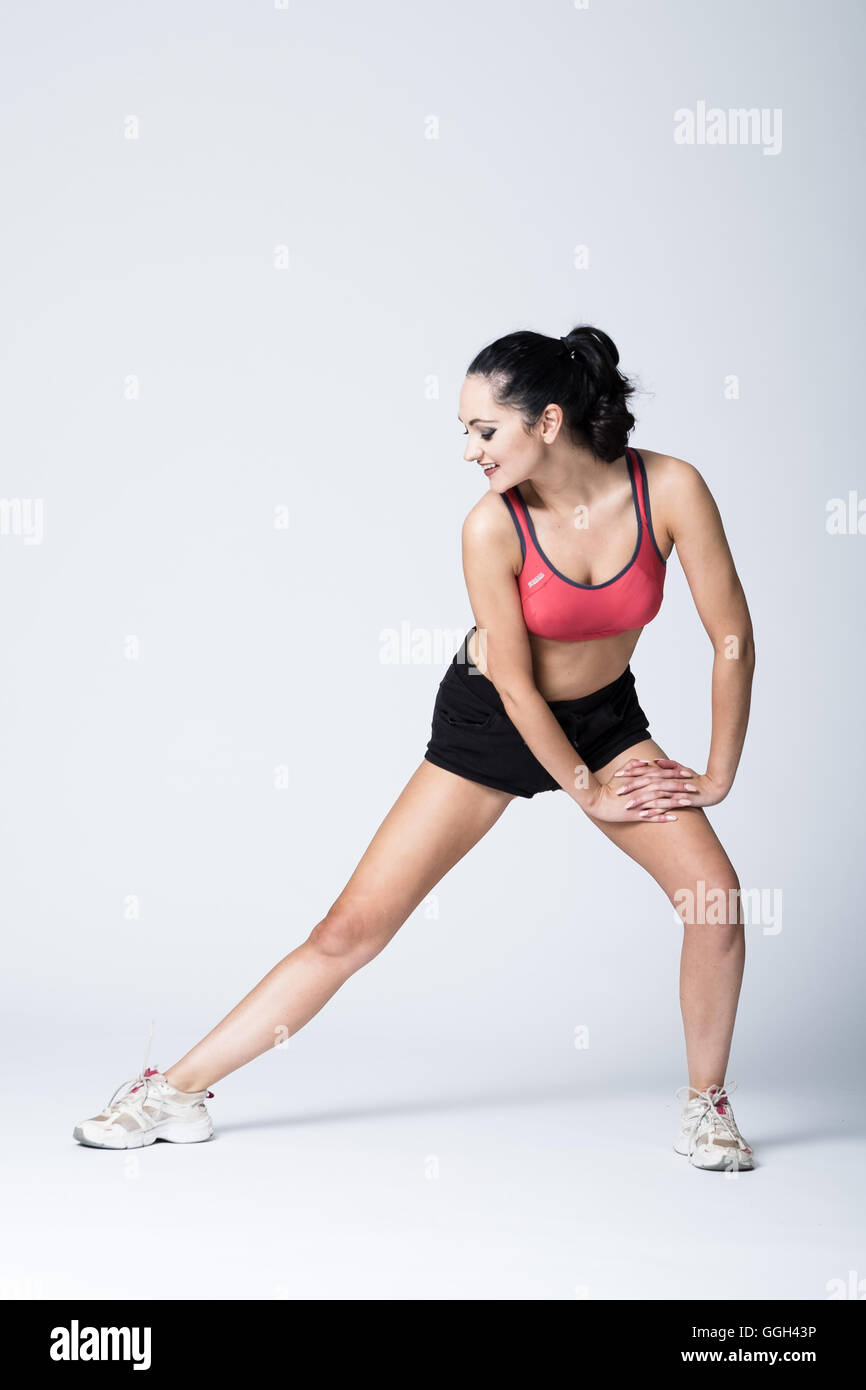 Donna nella sua 20s in attrezzature fitness facendo pre-esercizio stretching Foto Stock