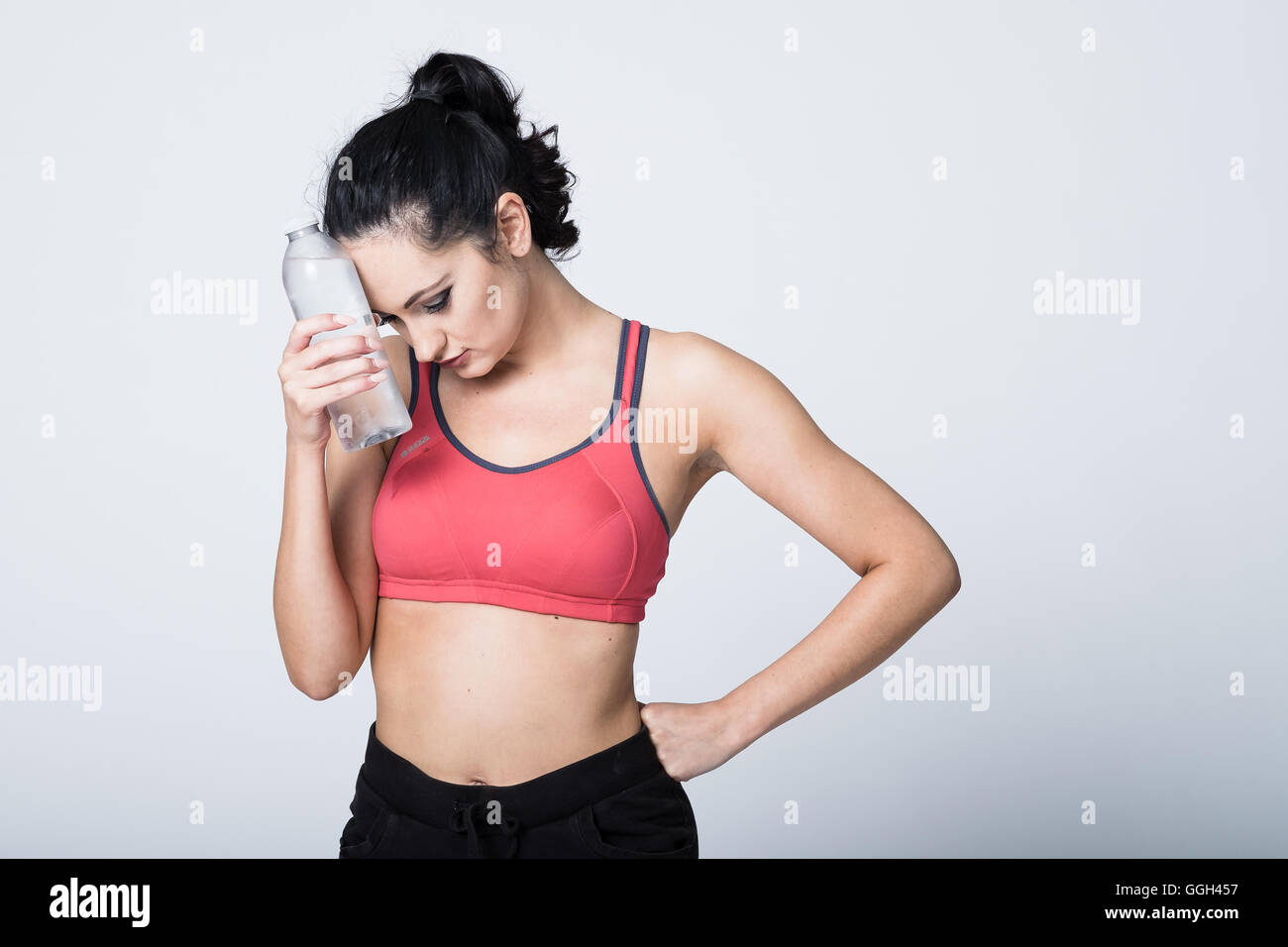 Donna nella sua 20s in attrezzature fitness il raffreddamento la fronte con una bottiglia di acqua raffreddata dopo il lavoro e di esercizio. Foto Stock