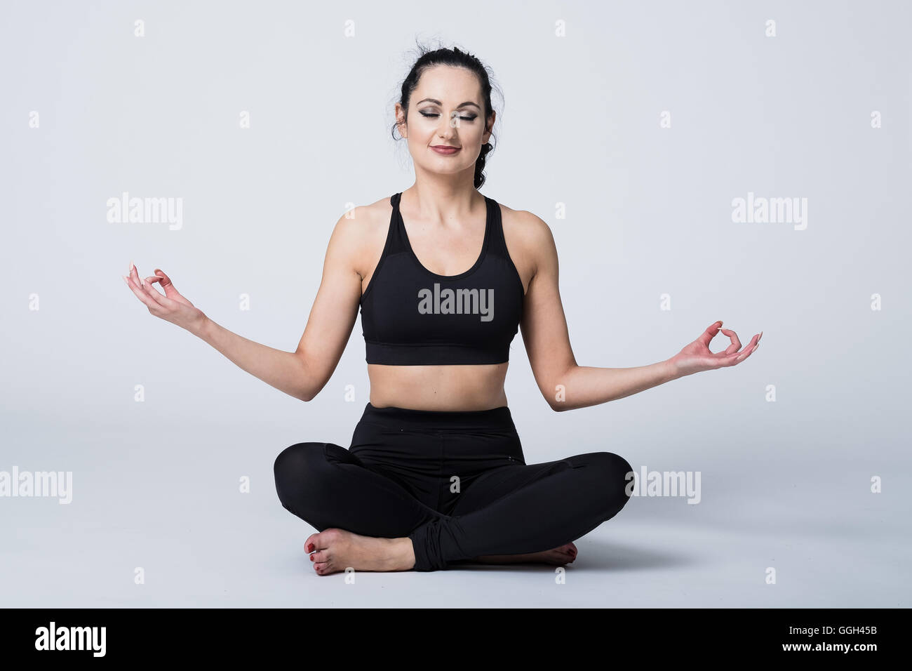 Donna nella sua 20s in attrezzature fitness pratica yogic meditando nella posizione del loto Foto Stock