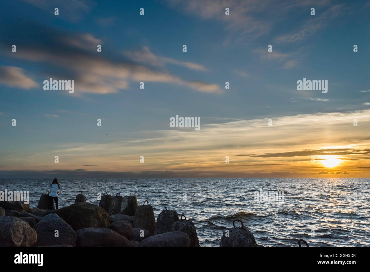 Donna che guarda al tramonto al mare pieno di rocce Foto Stock