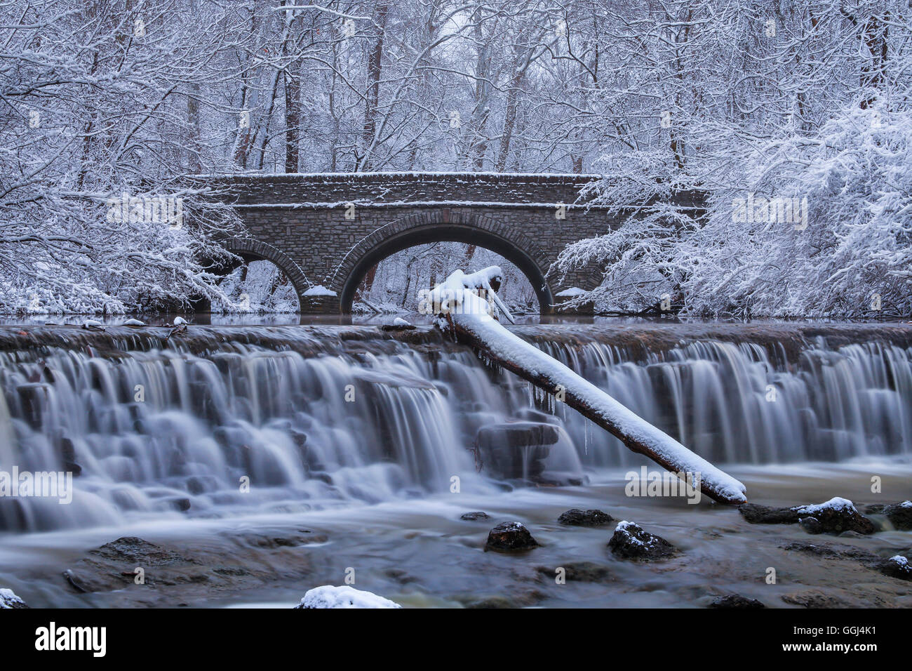 Coperta di neve alberi che incornicia un ponte di pietra e cascata durante l'Inverno nel parco, Sharon boschi, Southwestern Ohio, Stati Uniti d'America Foto Stock