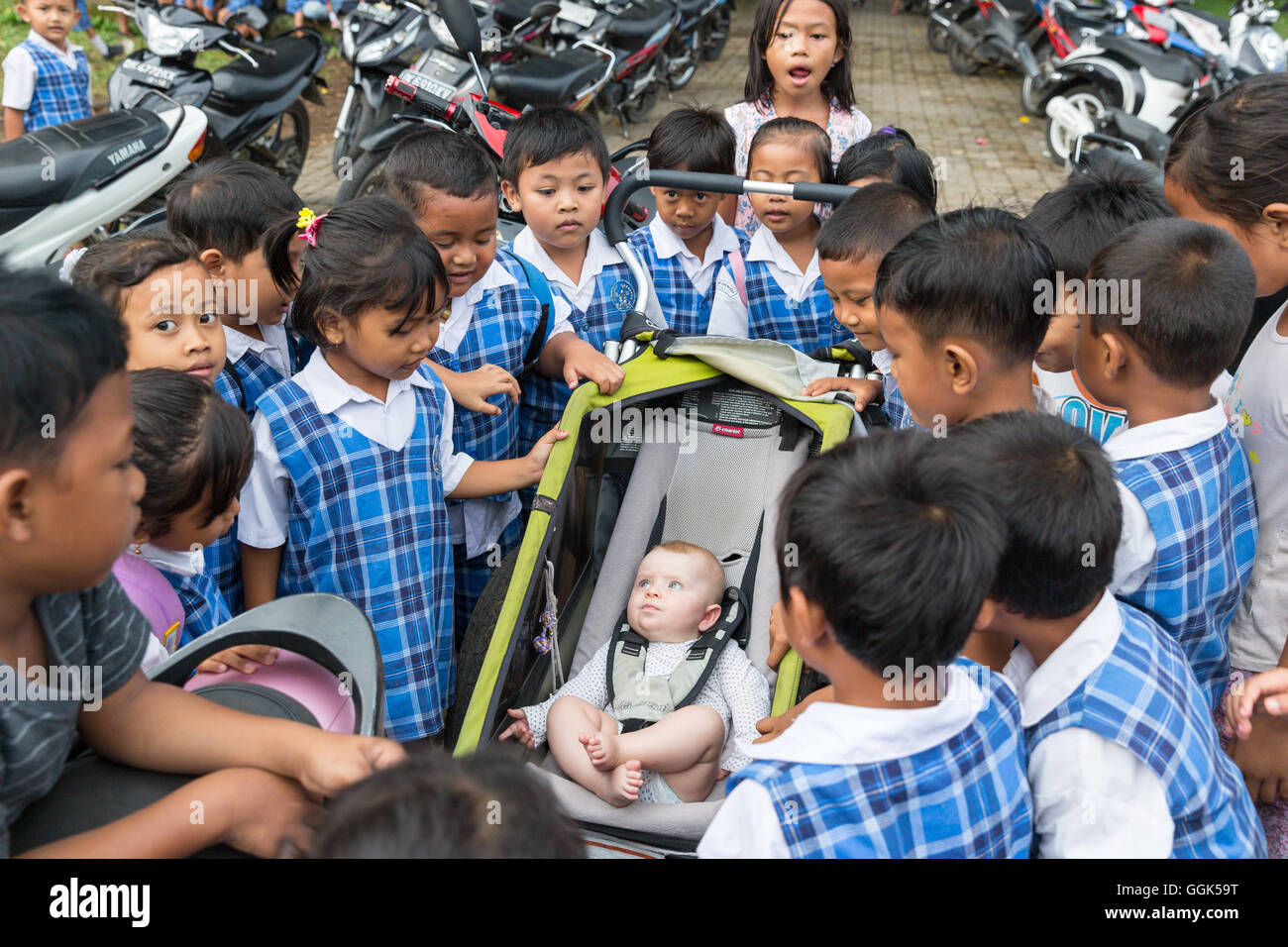 Molti allievi Balinese essendo curioso circa western baby, ragazza 5 mesi di età, seduta in un passeggino, bambini raccogliendo intorno, Foto Stock