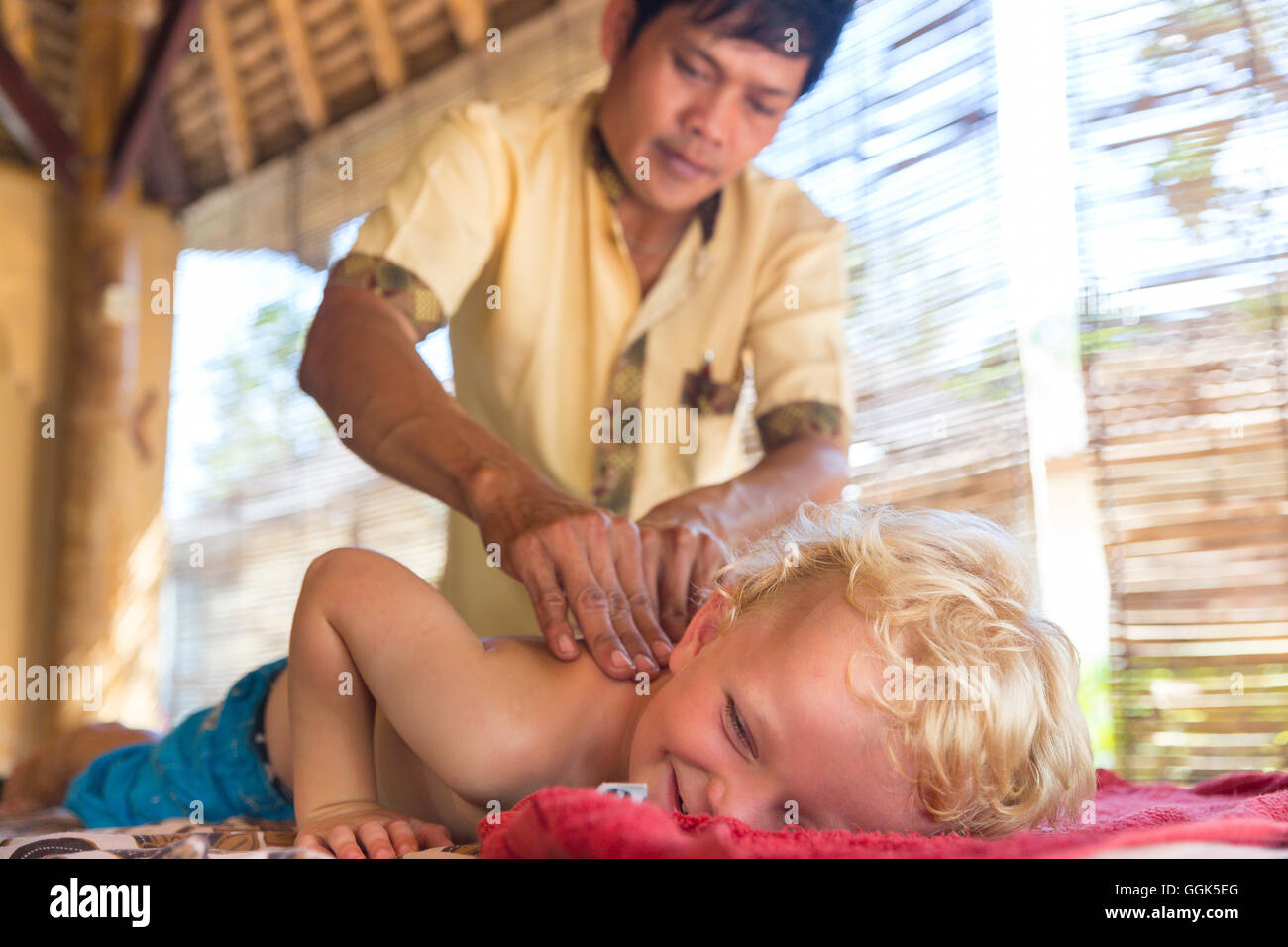 Little Boy getting massaggio alla schiena, massaggiatori Balinesi, ragazzo di 3 anni, benessere, hotel, contatto interculturale, incontro persone locali Foto Stock