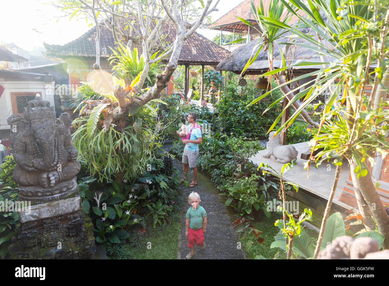 Balinese resort per vacanze in Ubud, padre con il bambino in braccio, 5 mesi, figlio,boy, 3 anni, bionda, giardino tropicale, scultura Ganesha, Foto Stock