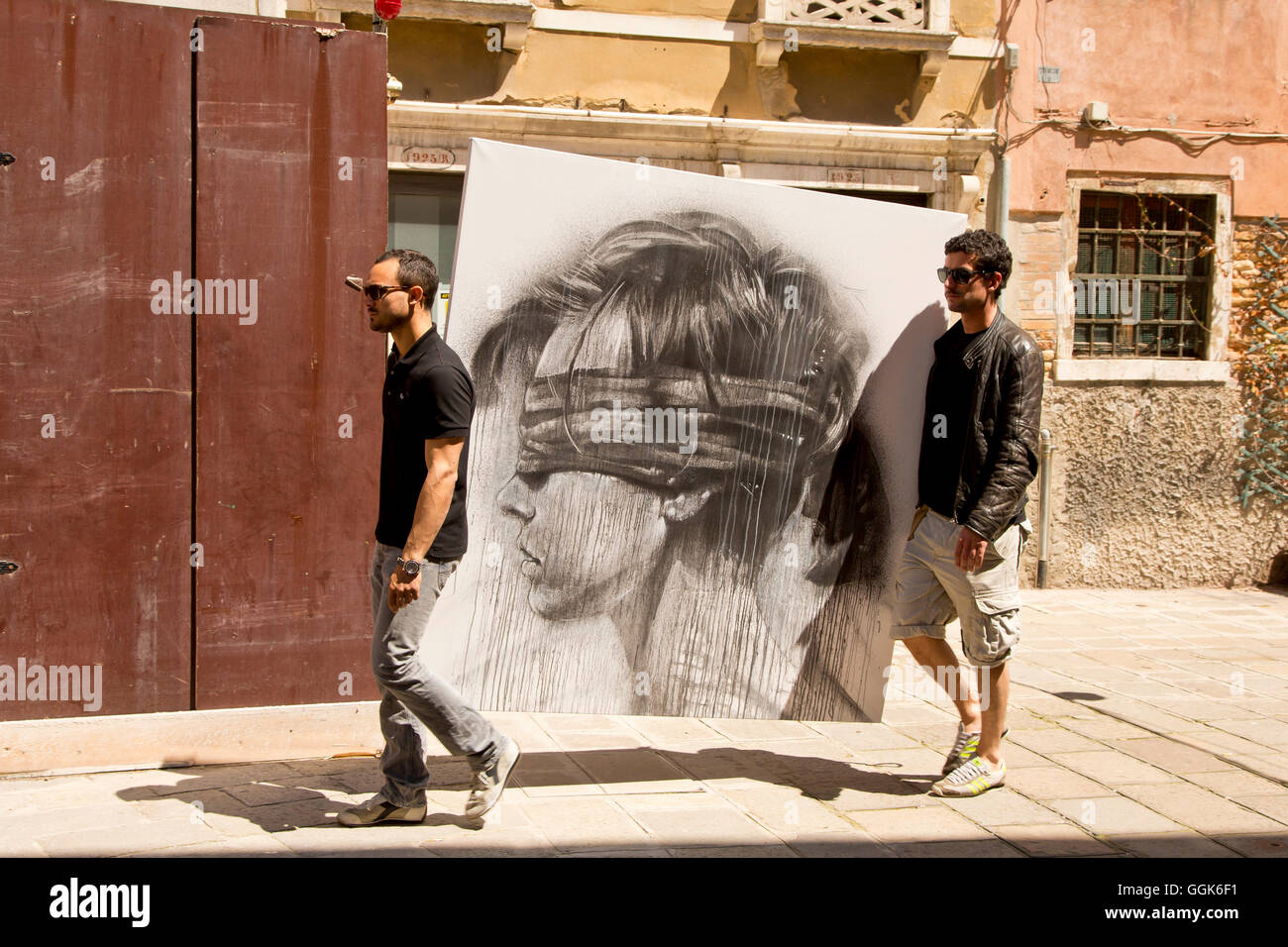 Due giovani uomini che trasportano un enorme disegno dotato di una testa di donna con gli occhi bendati lungo un sentiero vicino a Campo Sant Stefano, Venezia, V Foto Stock