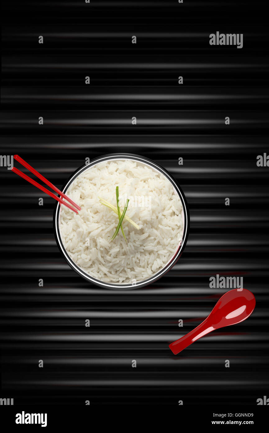 Bacchette in una ciotola di riso in bianco con cucchiaio rosso Foto Stock