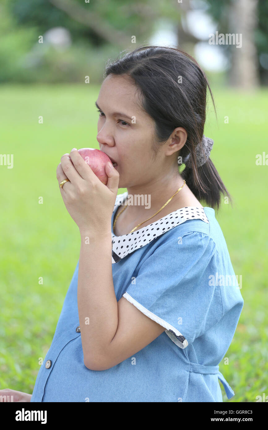 Asian Le donne in gravidanza con mano apple di cattura fino a mangiare nel parco pubblico. Foto Stock
