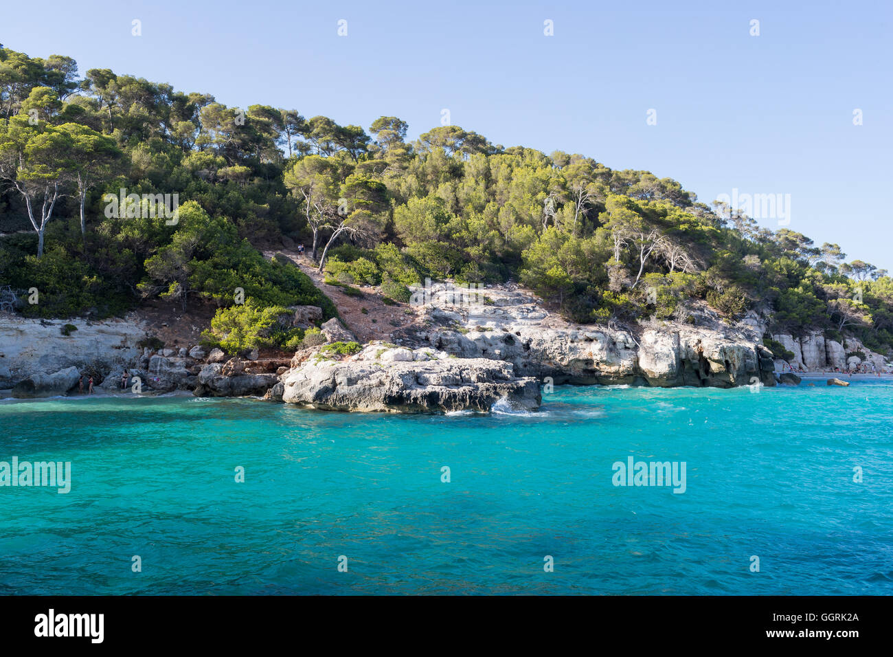 Baia con acqua blu cristallina circondata da scogliere e da alberi di pino Foto Stock