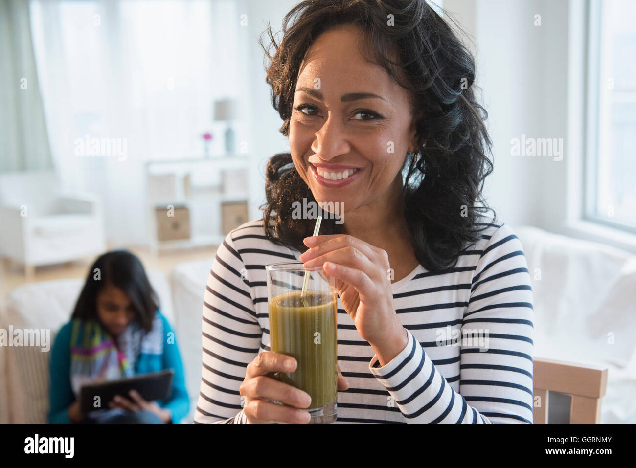 Madre bere frullato verde mentre la figlia utilizza tavoletta digitale Foto Stock