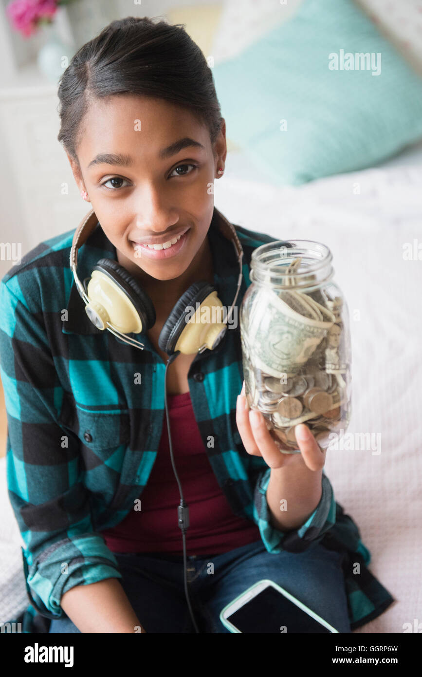 Razza mista ragazza con vaso contenente denaro contante e delle monete metalliche in euro Foto Stock