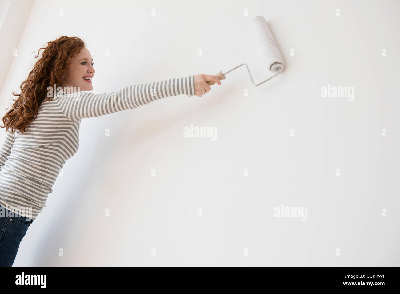 La donna caucasica muro dipinto di bianco con rullo di vernice Foto Stock