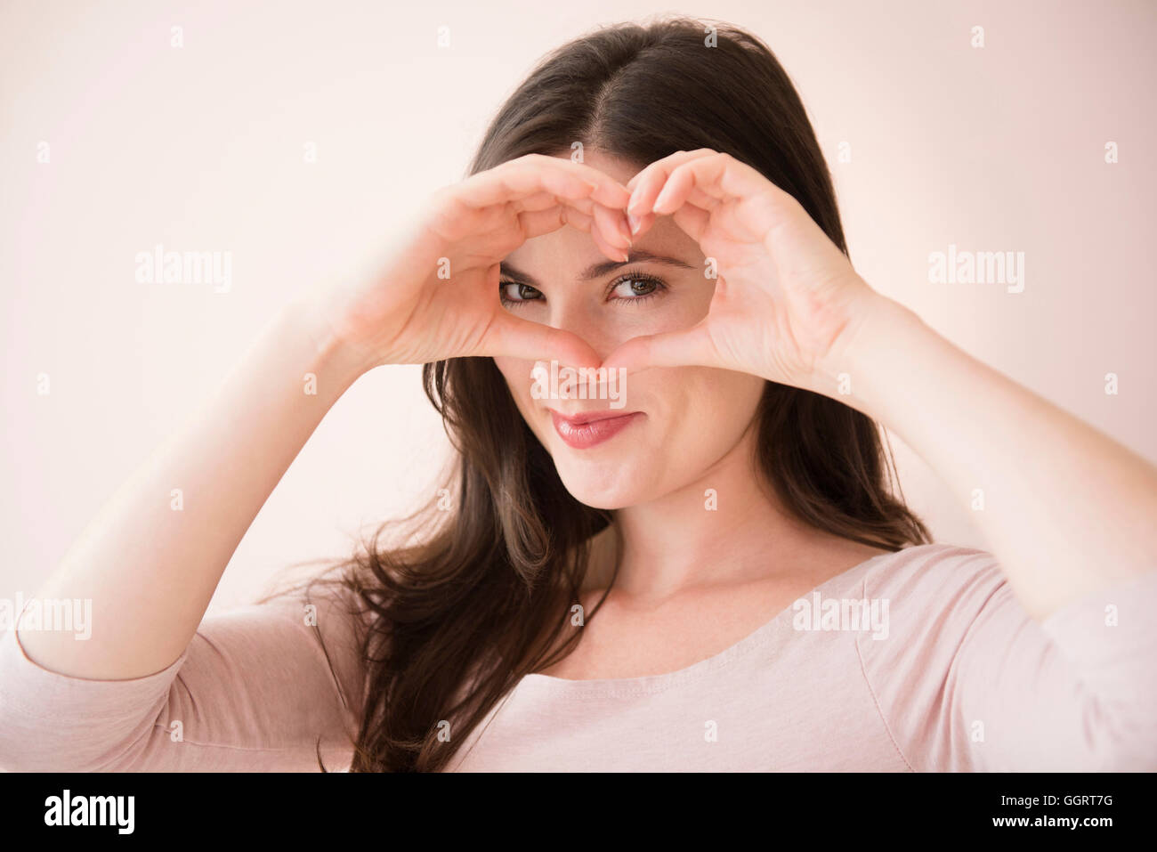 La donna caucasica gesticolando cuore-forma con le mani sopra gli occhi Foto Stock
