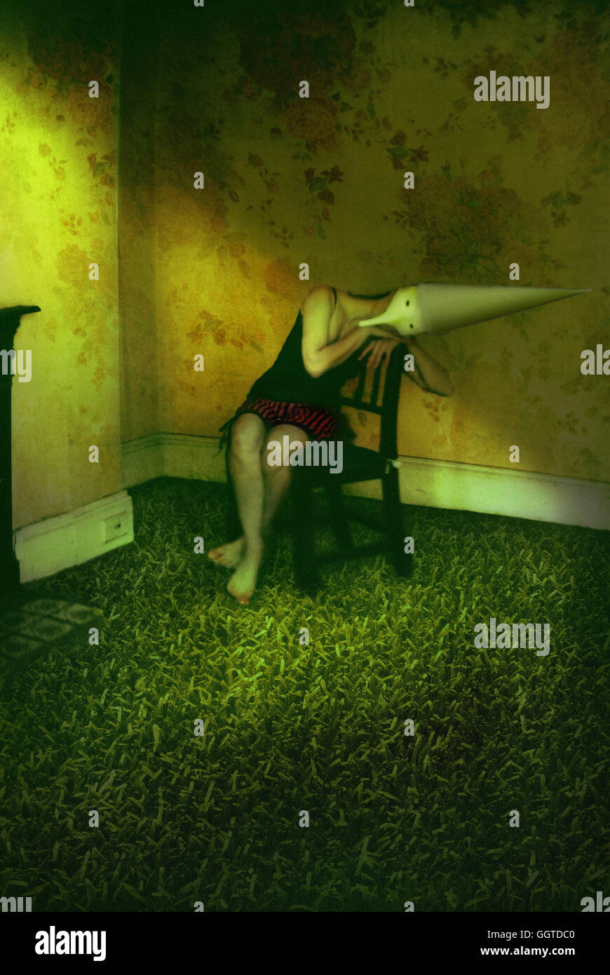 Surreale Ritratto di giovane donna che indossa il cono hat seduti su una sedia in camera riempita con erba Foto Stock