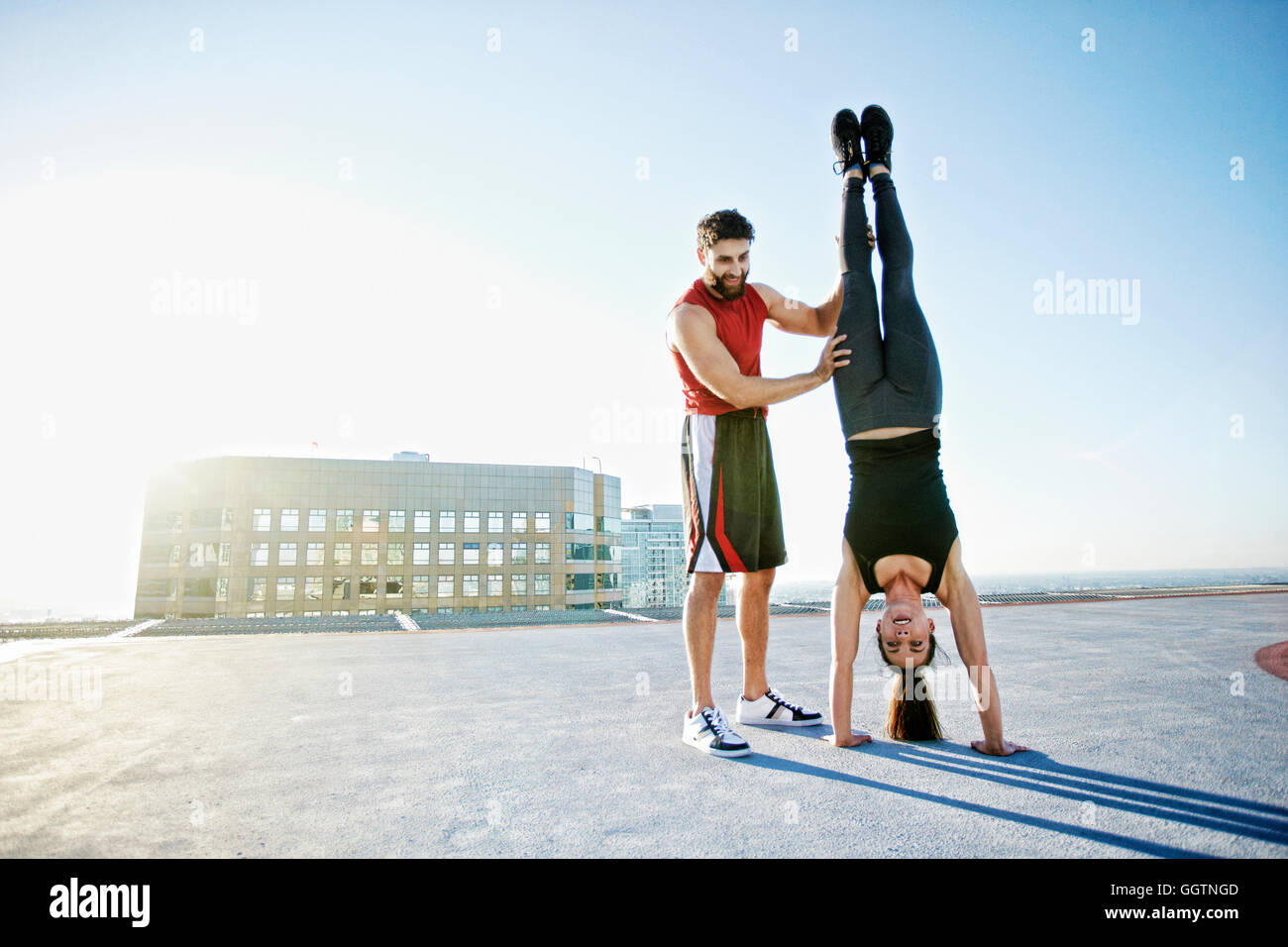 Uomo caucasico aiutando donna fare handstand sul tetto urbano Foto Stock