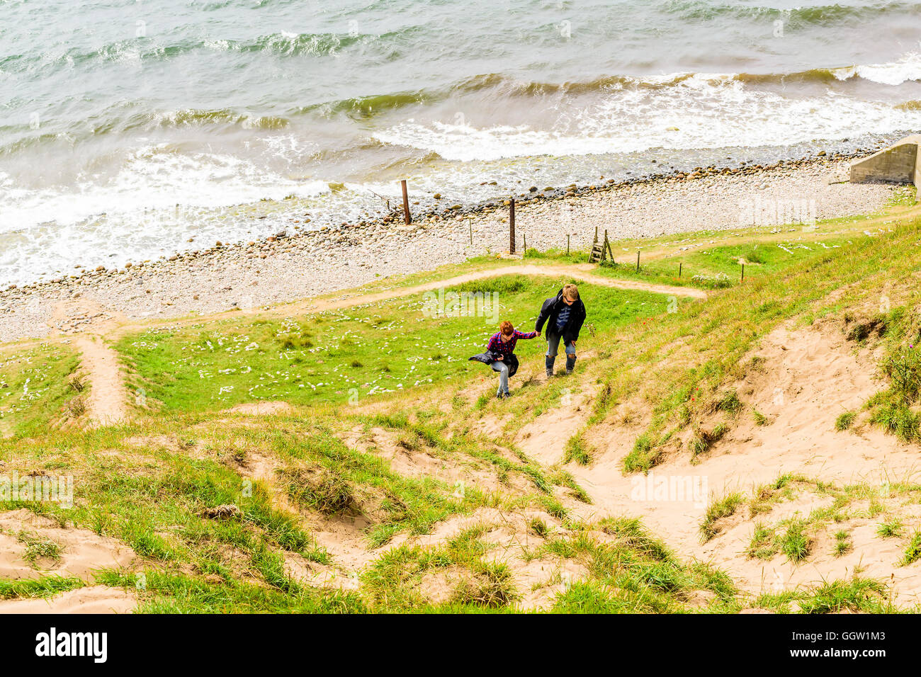 Kaseberga, Svezia - 1 Agosto 2016: giovane adulto uomo aiutando una donna salire una ripida collina di sabbia dall'oceano sotto. La vita reale sit Foto Stock