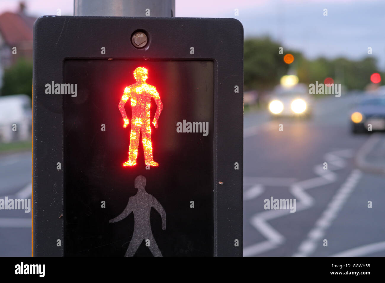 Uomo rosso a UK Pelican Crossing, con traffico di sera in background Foto Stock