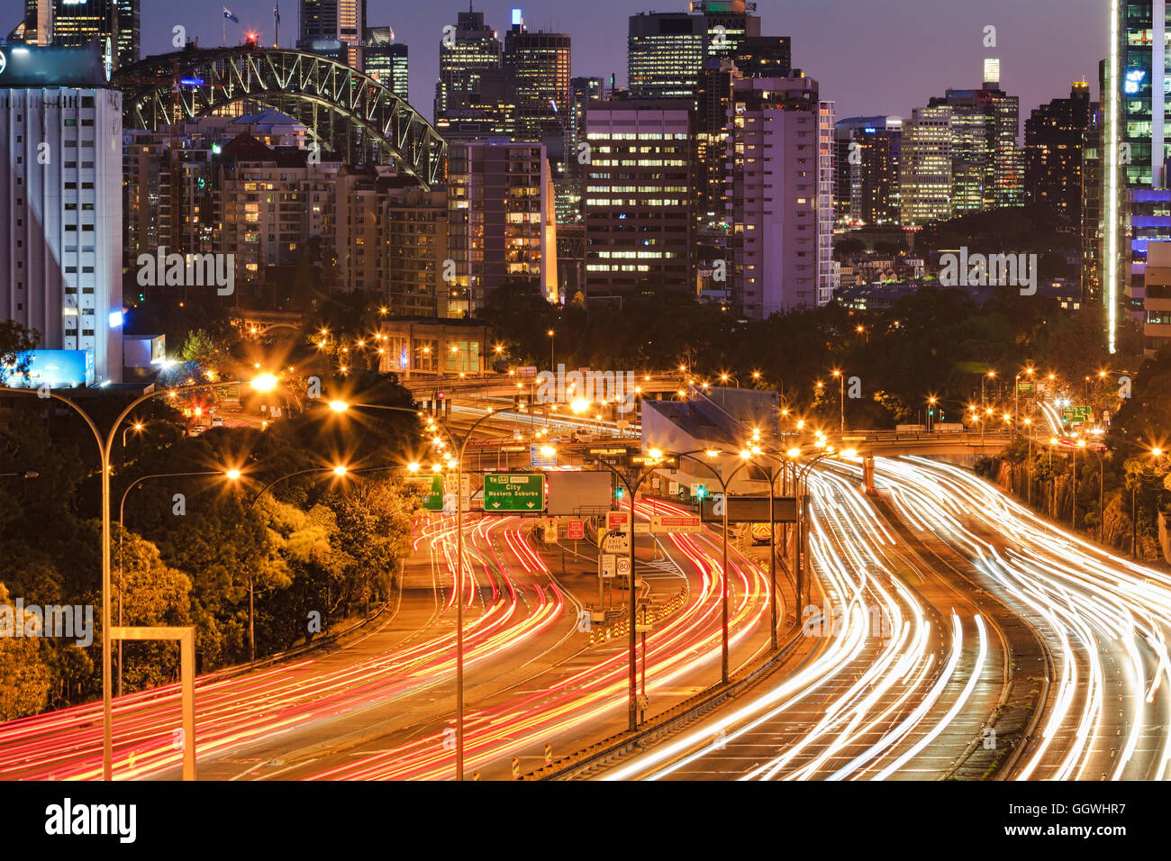 Multi-lane warringah freeway a Sydney contro lo zoom in arcata del ponte e torri grattacielo al tramonto. Luci sfocate del proiettore Foto Stock