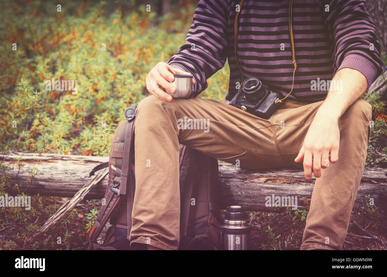 Uomo viaggiatore rilassante nella foresta con fotocamera, zaino e thermos bere il tè di viaggio il concetto di stile di vita le vacanze estive o Foto Stock