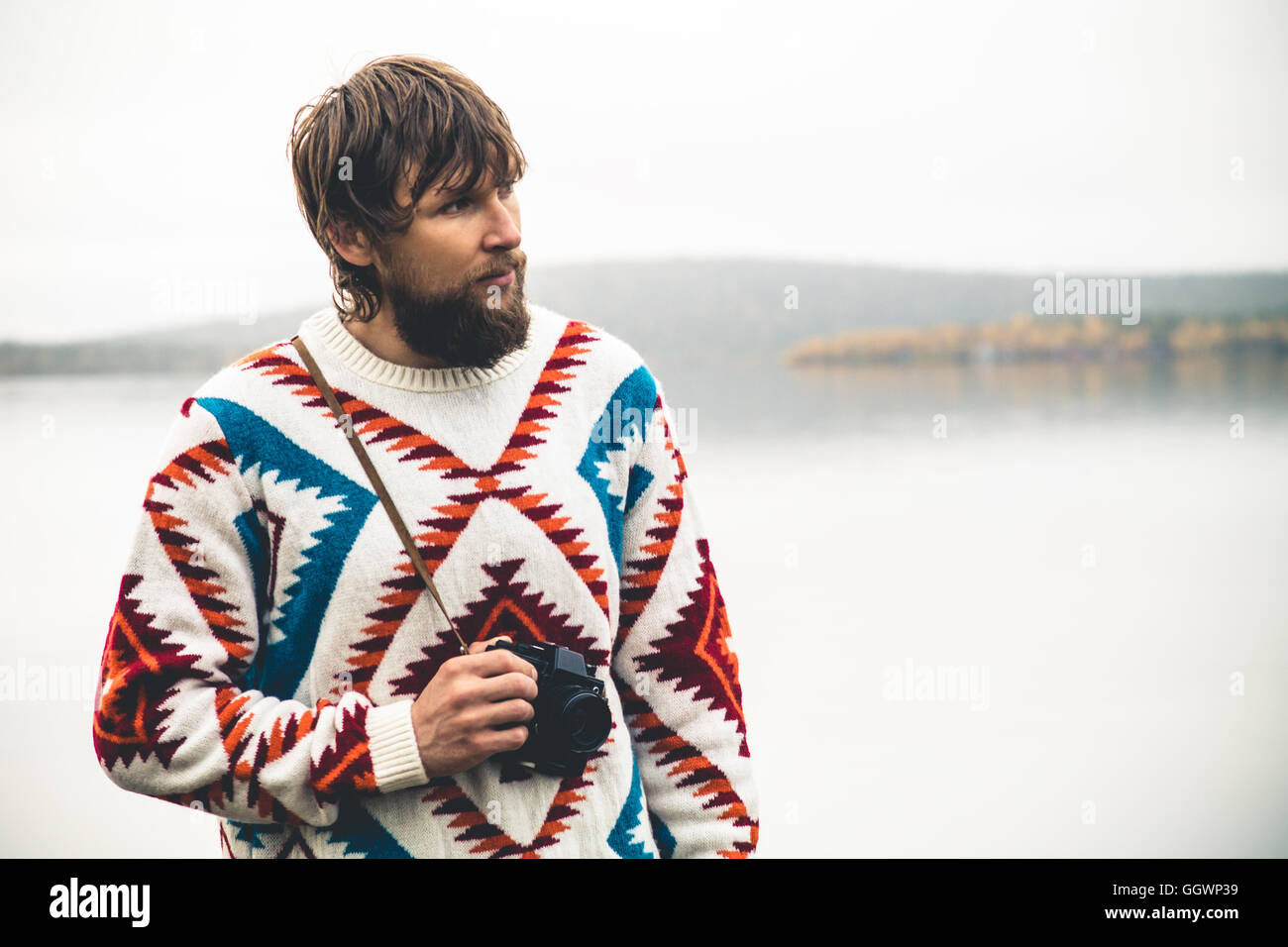 Giovane uomo barbuto con retrò fotocamera foto di moda stile di vita viaggio indossare pullover a maglia abbigliamento outdoor foggy natura sul retro Foto Stock
