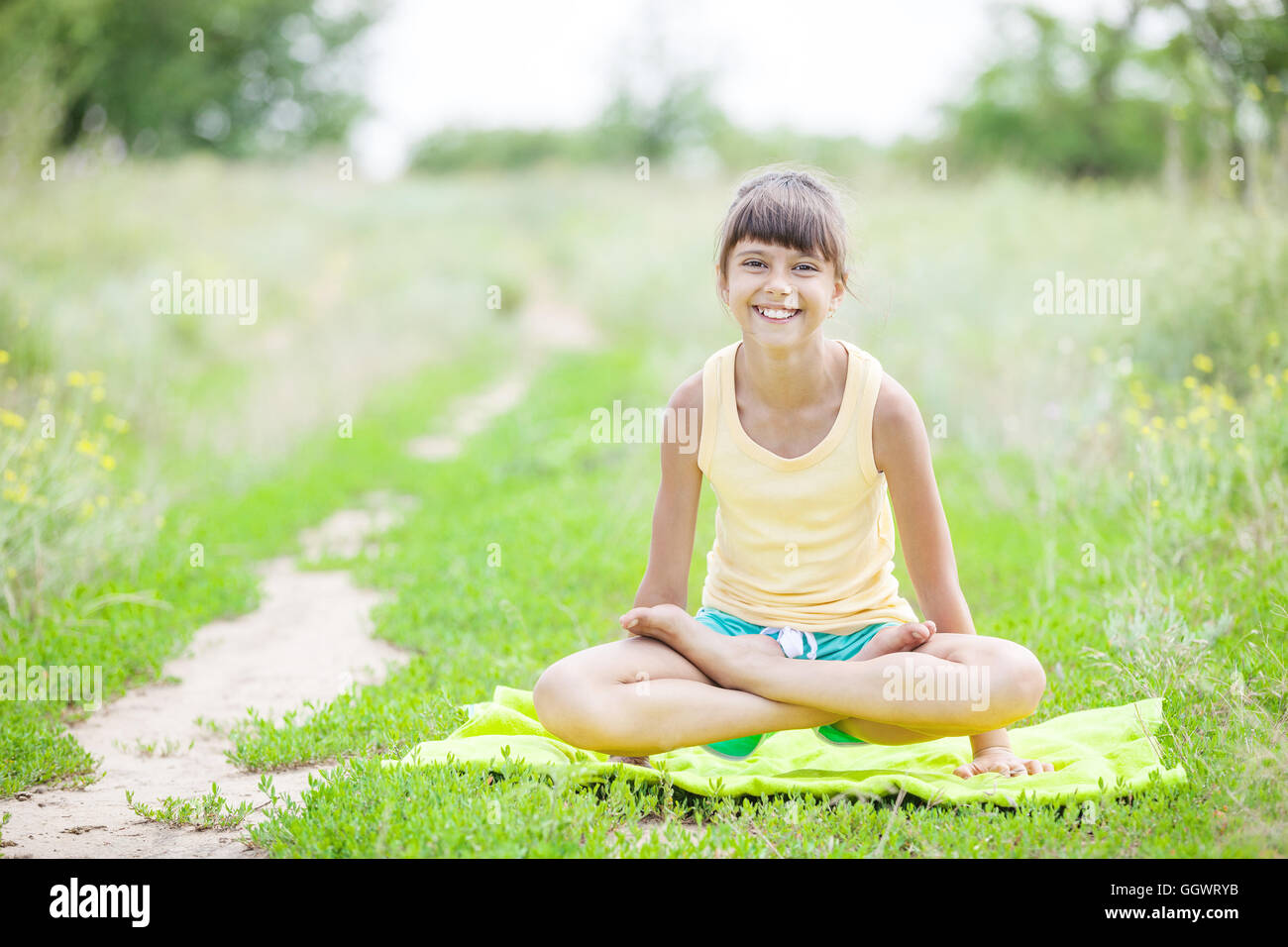 Giovane ragazza sorridente mentre è seduto nella posizione del loto all'aperto Foto Stock