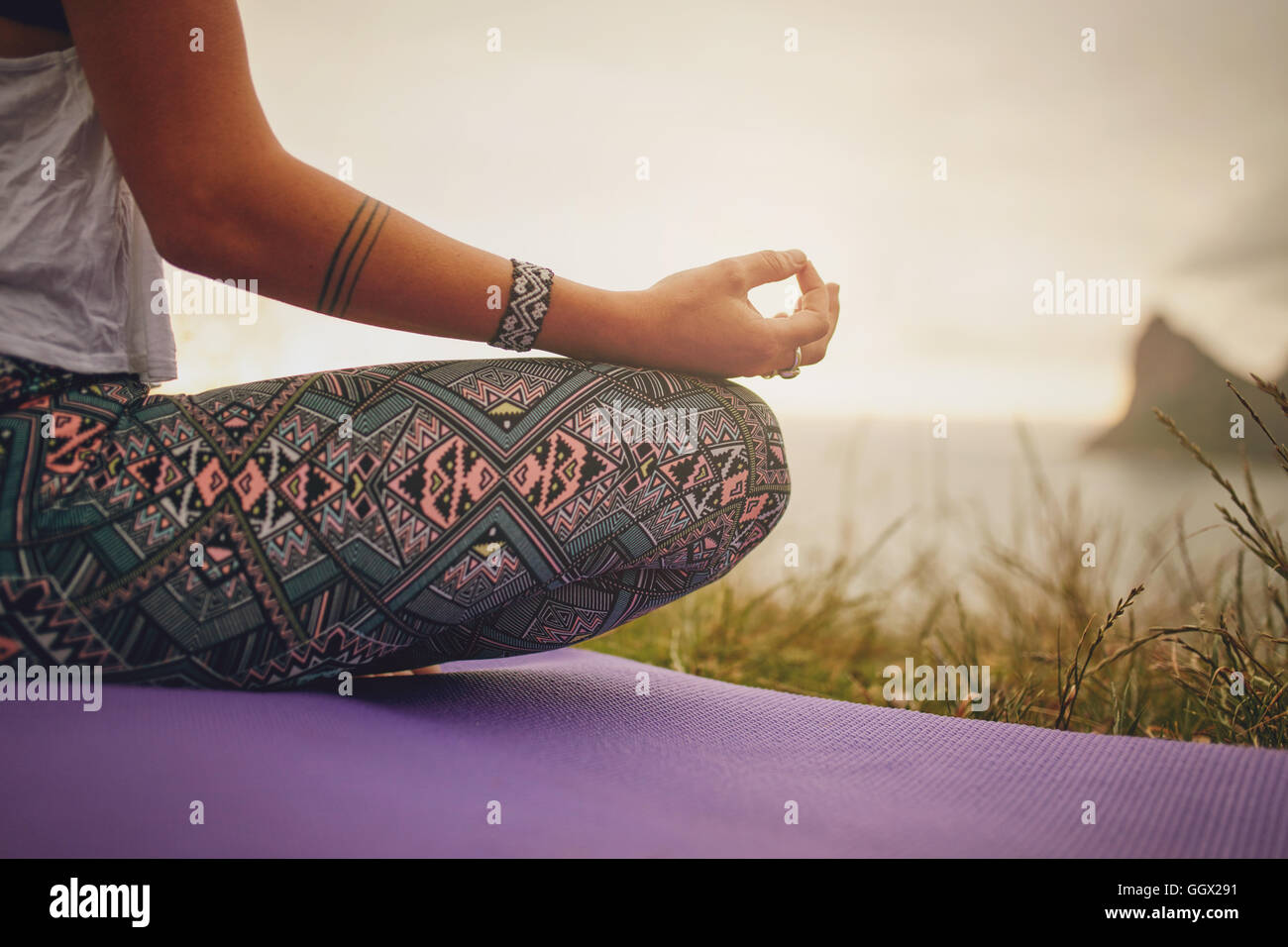 Foto ritagliata di donna seduta in posa di loto yoga sul tappetino per esercizi, con attenzione alle mani. fitness femminile in meditazione all'aperto. Foto Stock