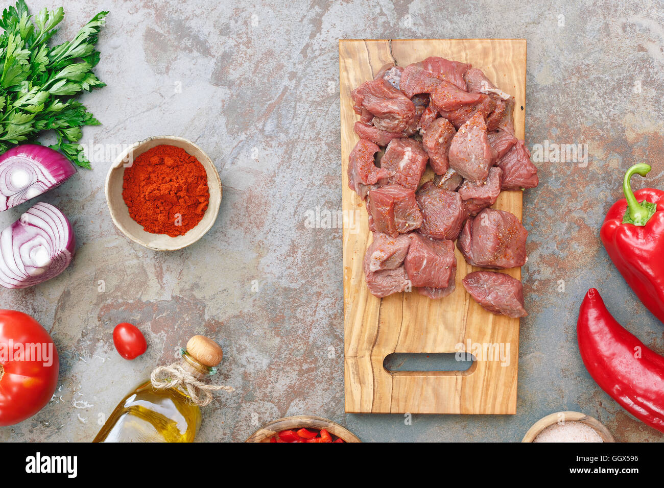 Carni bovine per gulasch. I cubetti di carne su un vecchio tagliere di legno e gli ingredienti per cucinare su sfondo rustico Foto Stock