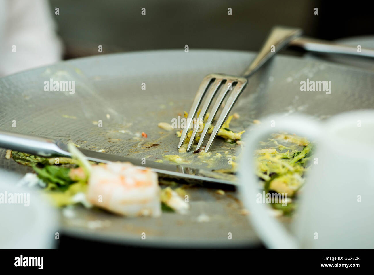 Cibo left overs su una piastra con un coltello e forchetta dopo la finitura di un pasto Foto Stock