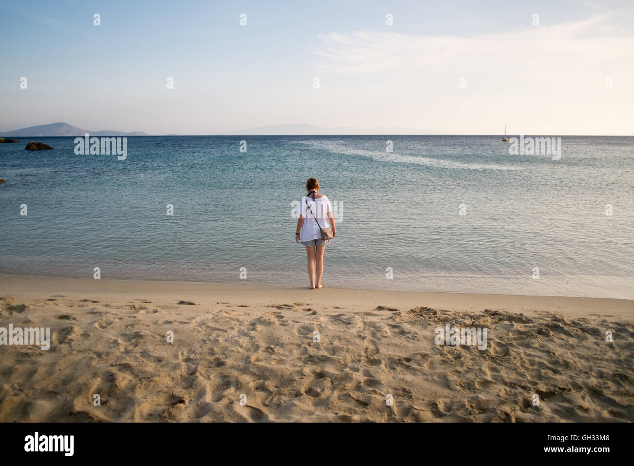 Vista posteriore della donna in piedi sulla spiaggia contro il mare e il cielo Foto Stock