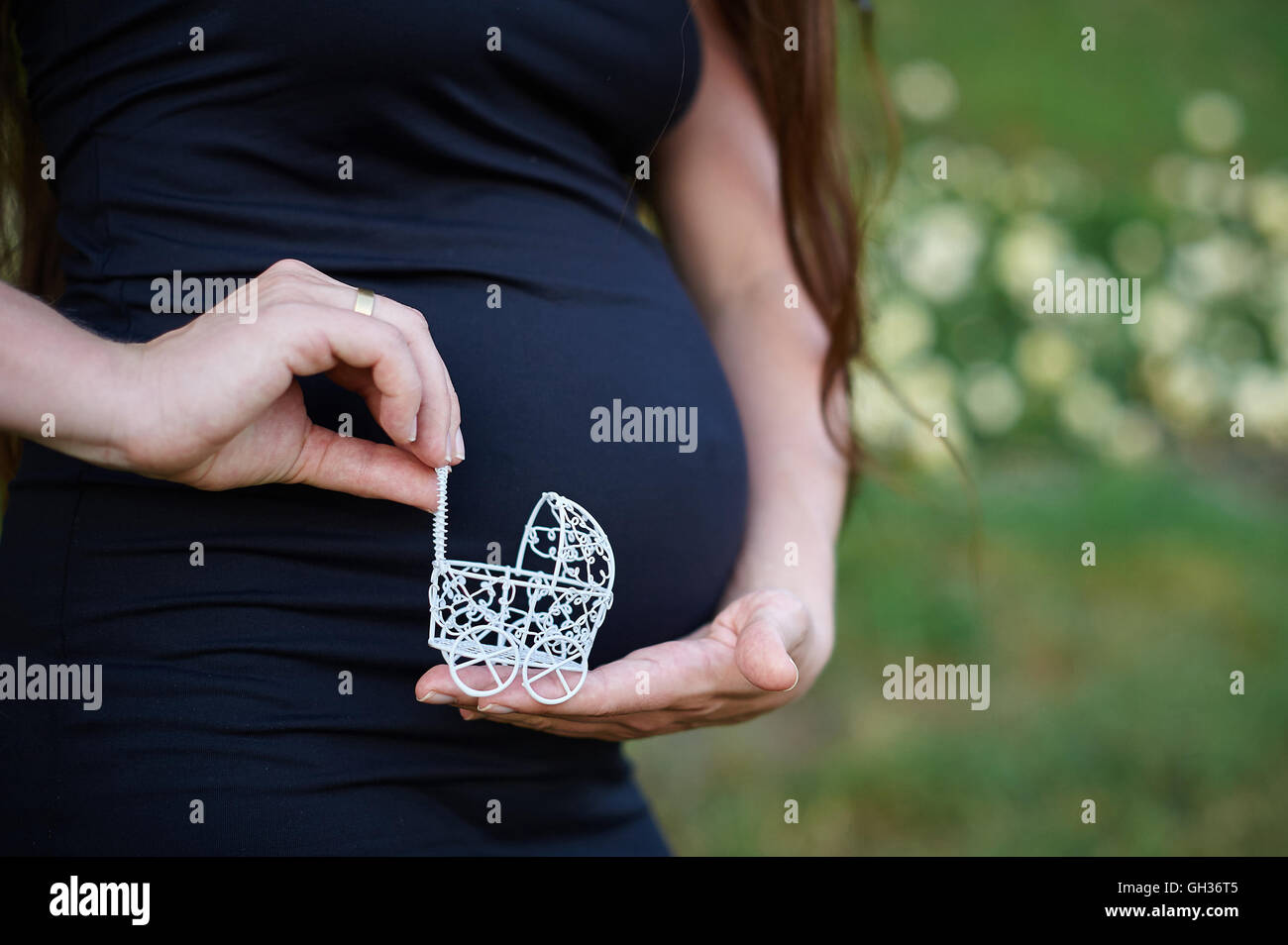 Concetto di gravidanza: ventre con mano azienda piccolo giocattolo passeggino Foto Stock