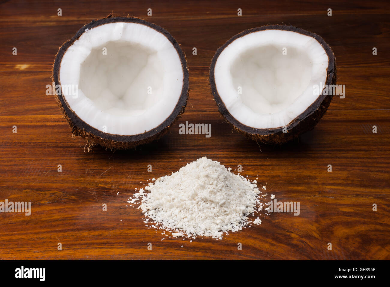 Una metà di noce di cocco con noce di cocco grattugiata riversandosi su di un tavolo di legno. Foto Stock