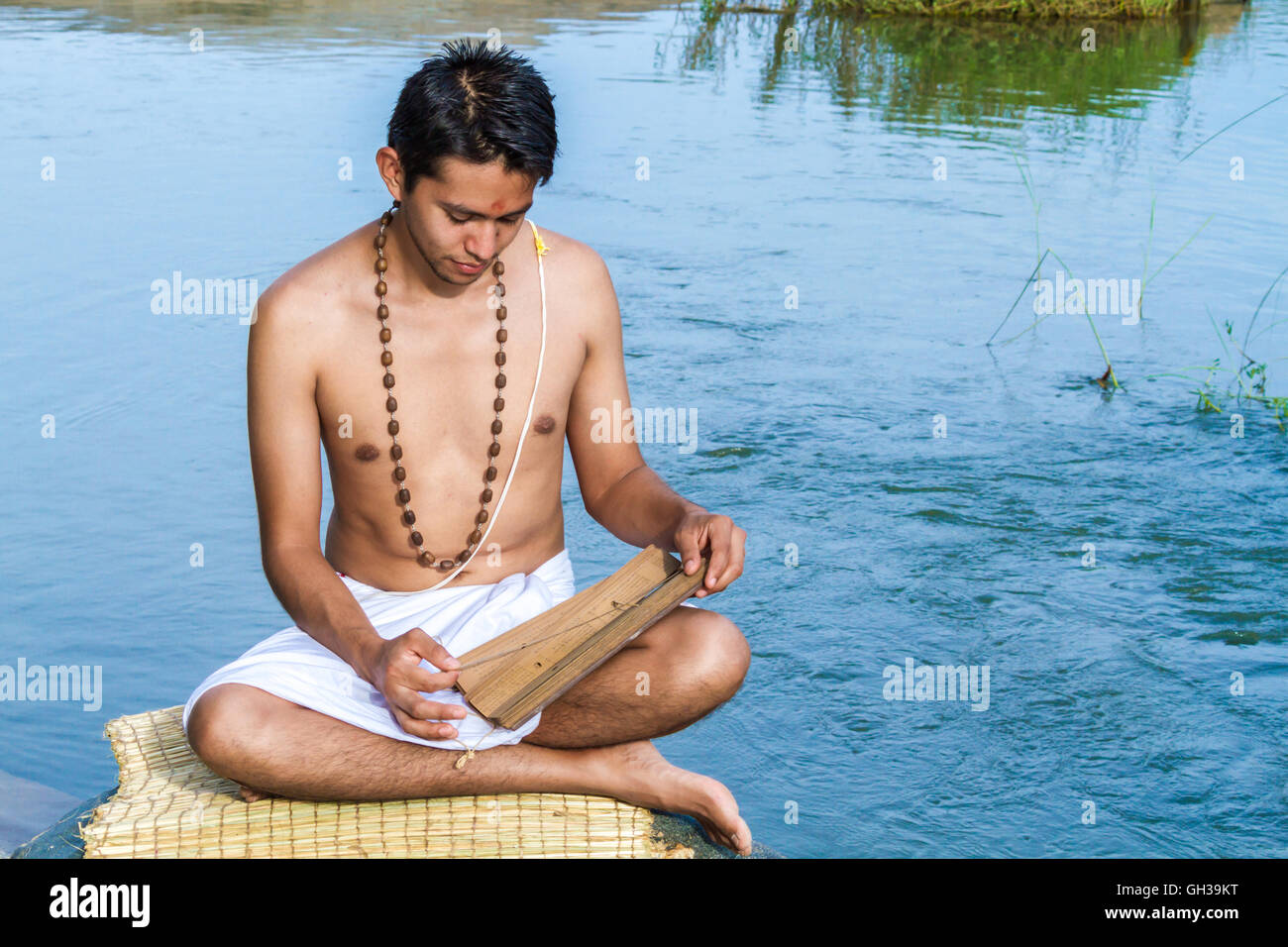 Un giovane bramino recita un antico palm indù-foglia di scrittura su una riva di un fiume. Foto Stock
