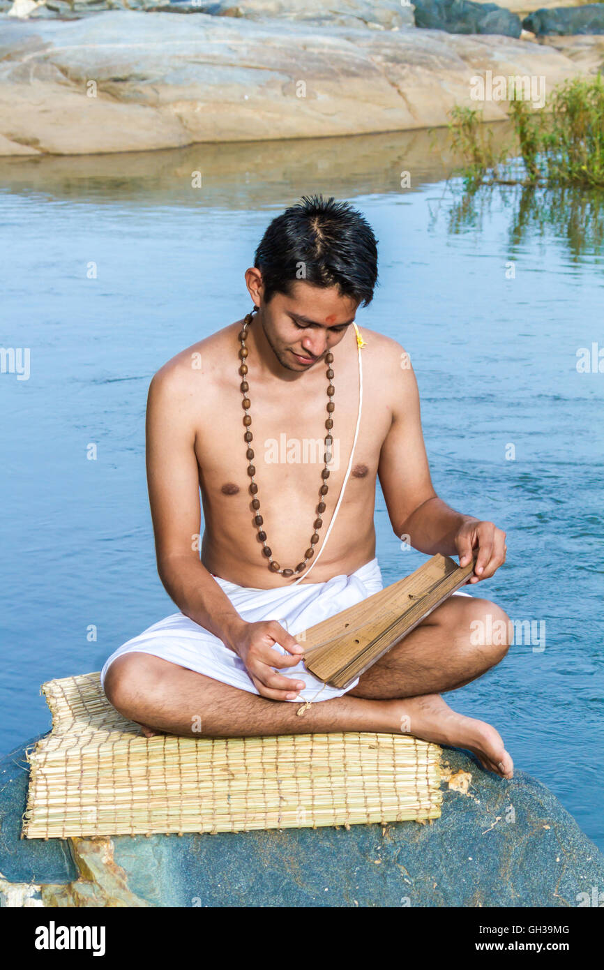 Un giovane bramino recita un antico palm indù-foglia di scrittura su una riva di un fiume. Foto Stock