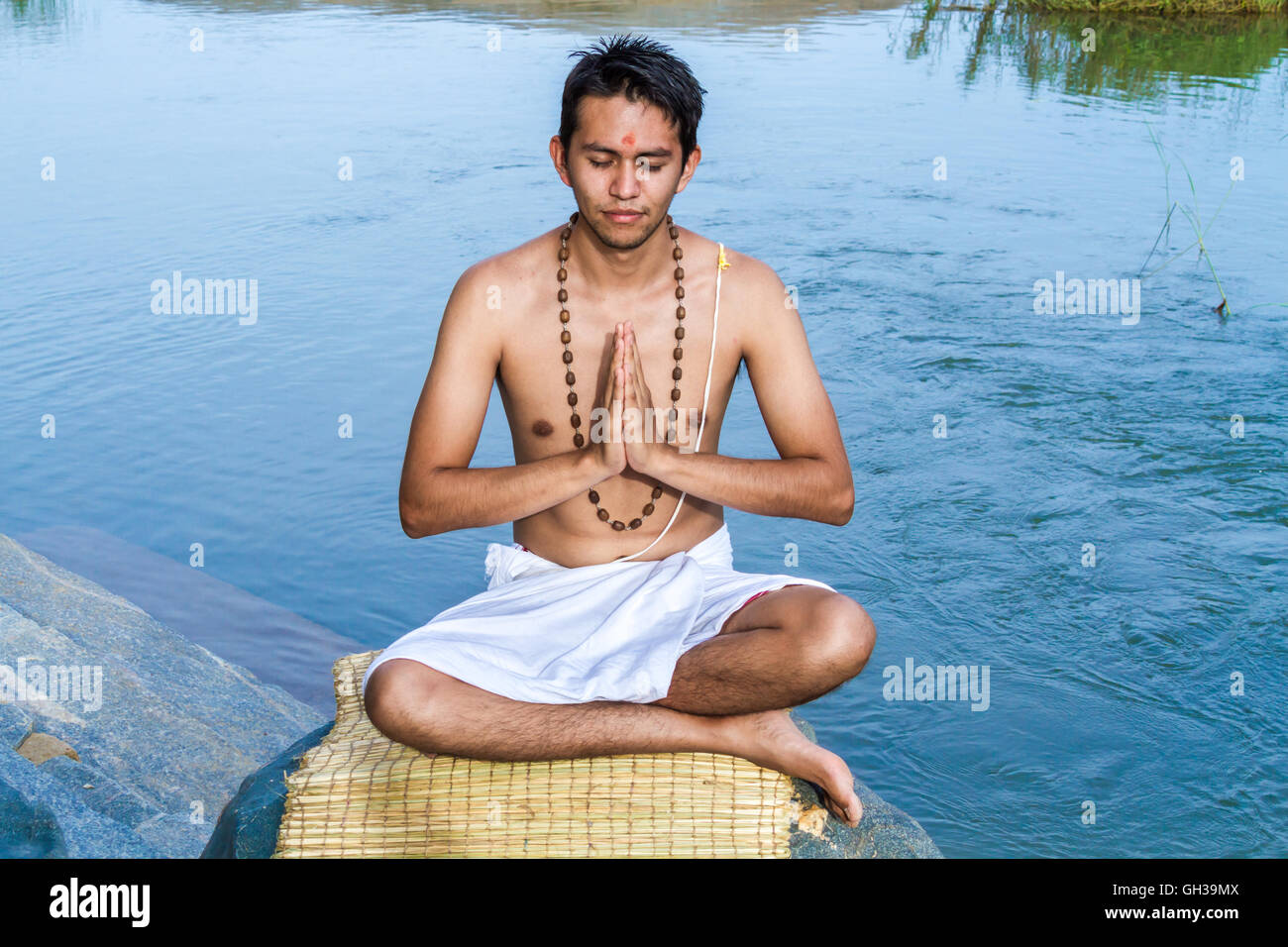 Un giovane sacerdote Indù (bramino) siede in preghiera sulle rive di un fiume. Foto Stock