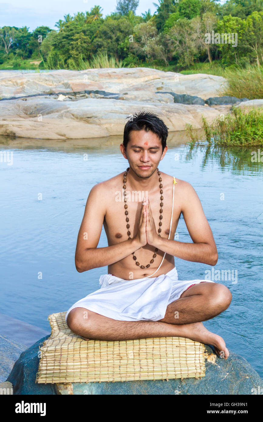 Un giovane sacerdote Indù (bramino) siede in preghiera sulle rive di un fiume. Foto Stock
