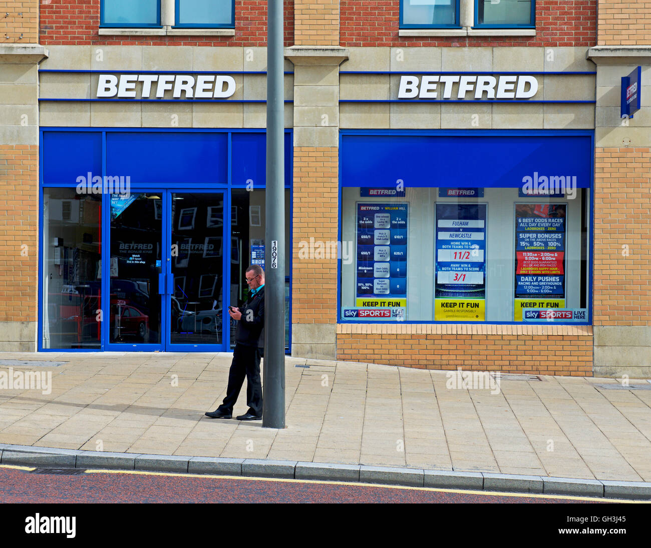 L'uomo puntella lampione esterno Betfred betting shop, England Regno Unito Foto Stock