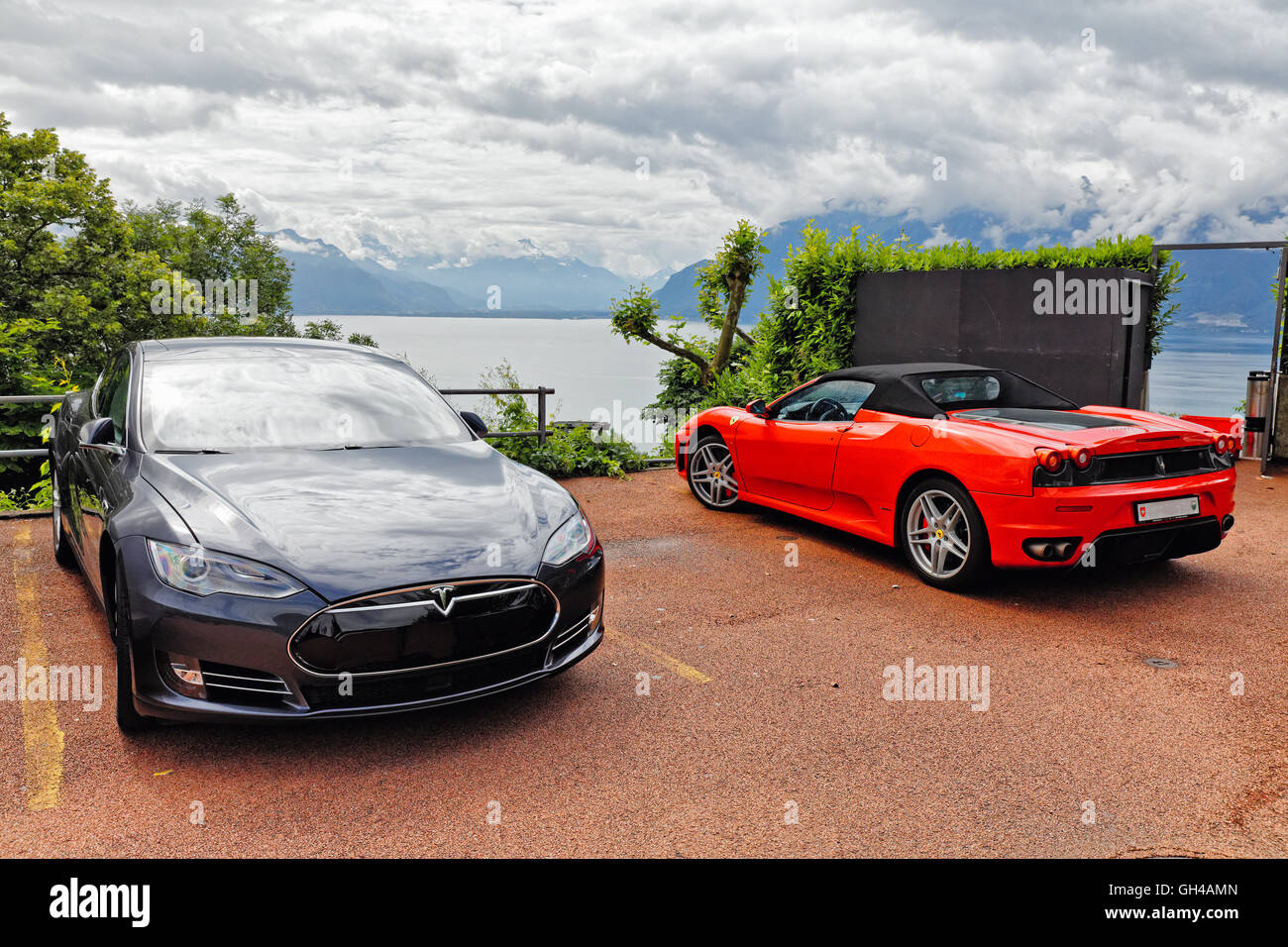 Una Tesla S berlina elettrica e un Rosso Ferrari cabrio auto parcheggiate in uno scenografico si affacciano sul lago di Ginevra, Chebrex, Vaud, CH Foto Stock