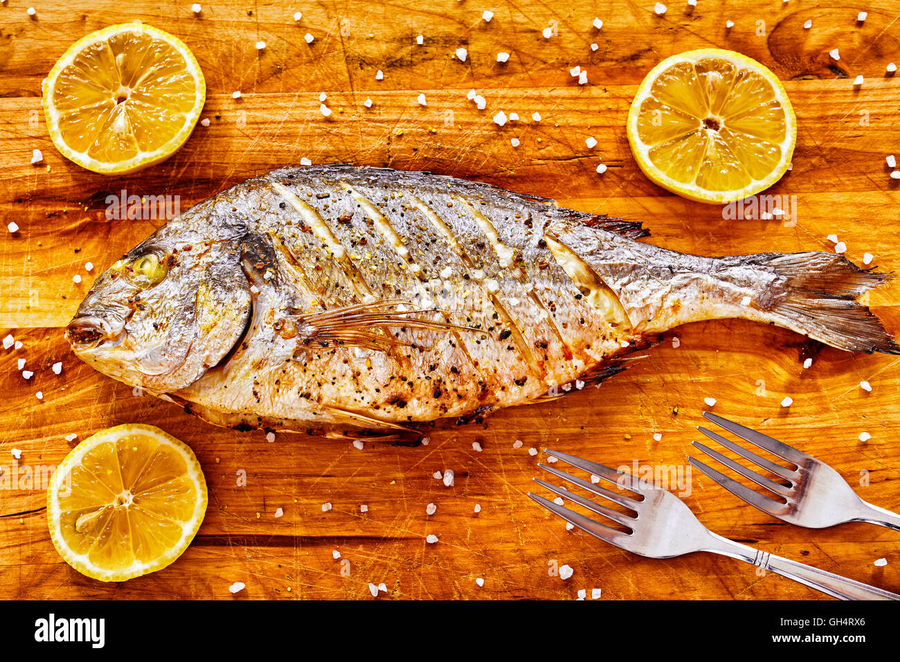 Arrosto testa dorato orate di pesce su un tavolo di legno con limoni e a grana grossa sale. Foto Stock