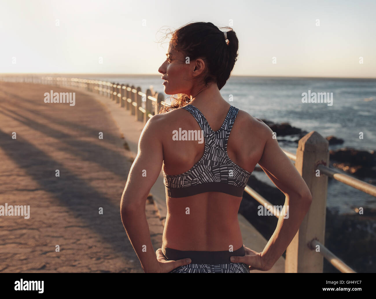 Vista posteriore immagine della donna fitness abbigliamento sportivo in piedi su un lungomare di distanza alla sera. Atleta femminile che guarda lontano con Foto Stock