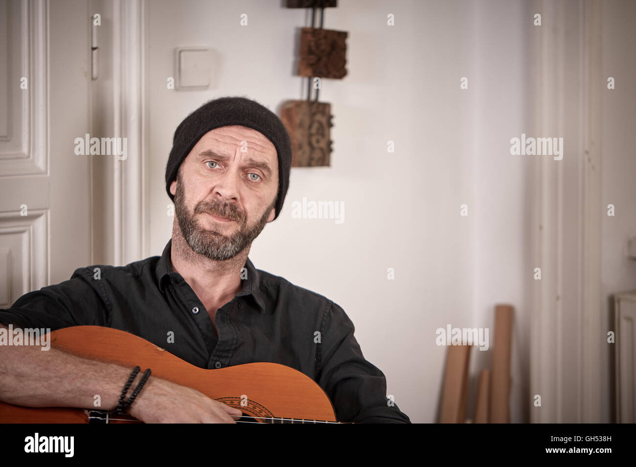Vecchio hiptser con la barba e hat tenendo una chitarra a casa seduti nella parte anteriore della porta Foto Stock