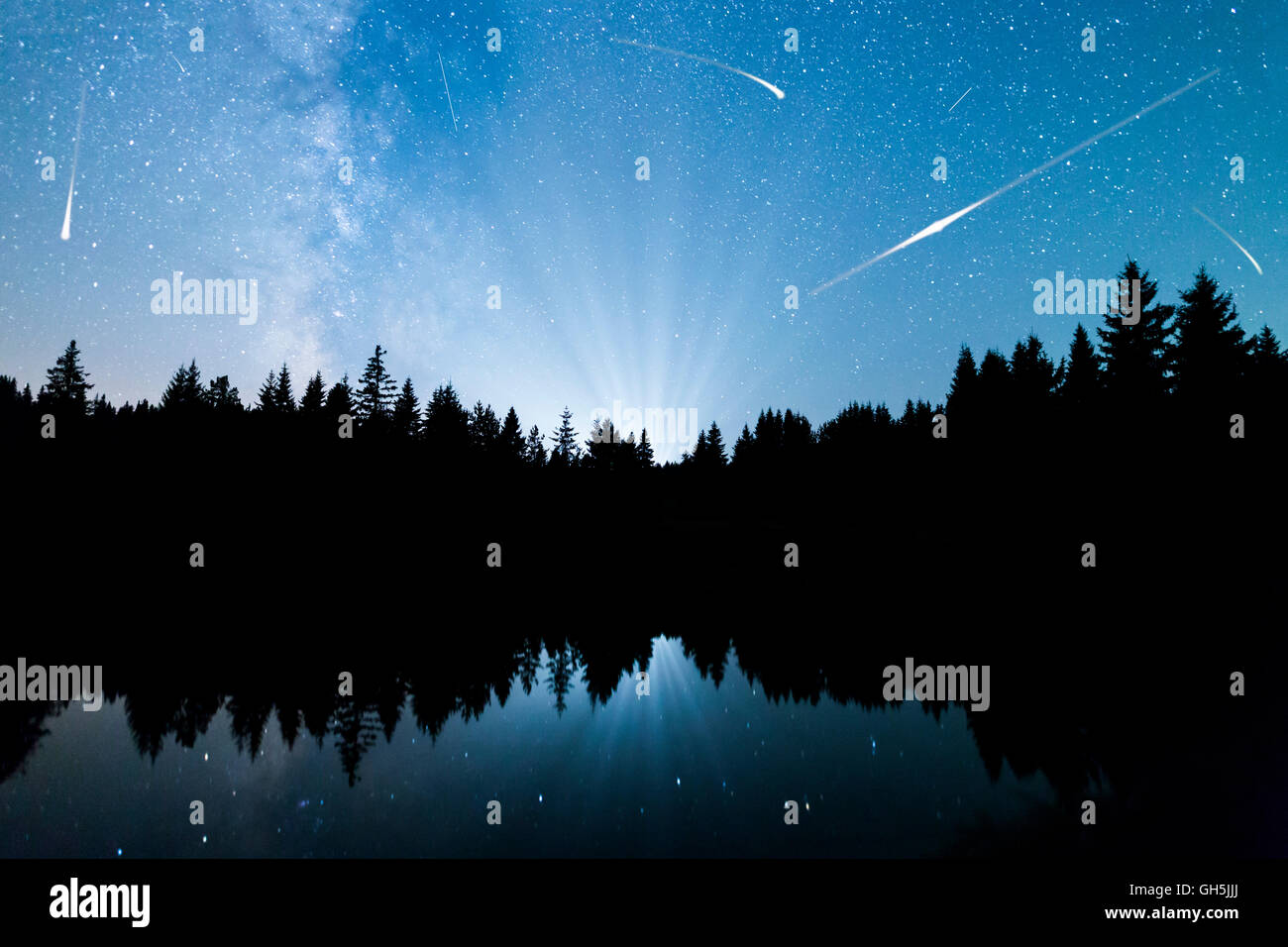 Una vista delle stelle della Via Lattea con una silhouette di una foresta di conifere in prossimità di un lago di montagna. Stelle cadenti riflettere Foto Stock