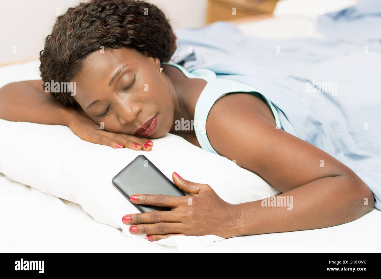 Bella donna che dorme nel letto con il suo telefono cellulare in mano Foto Stock