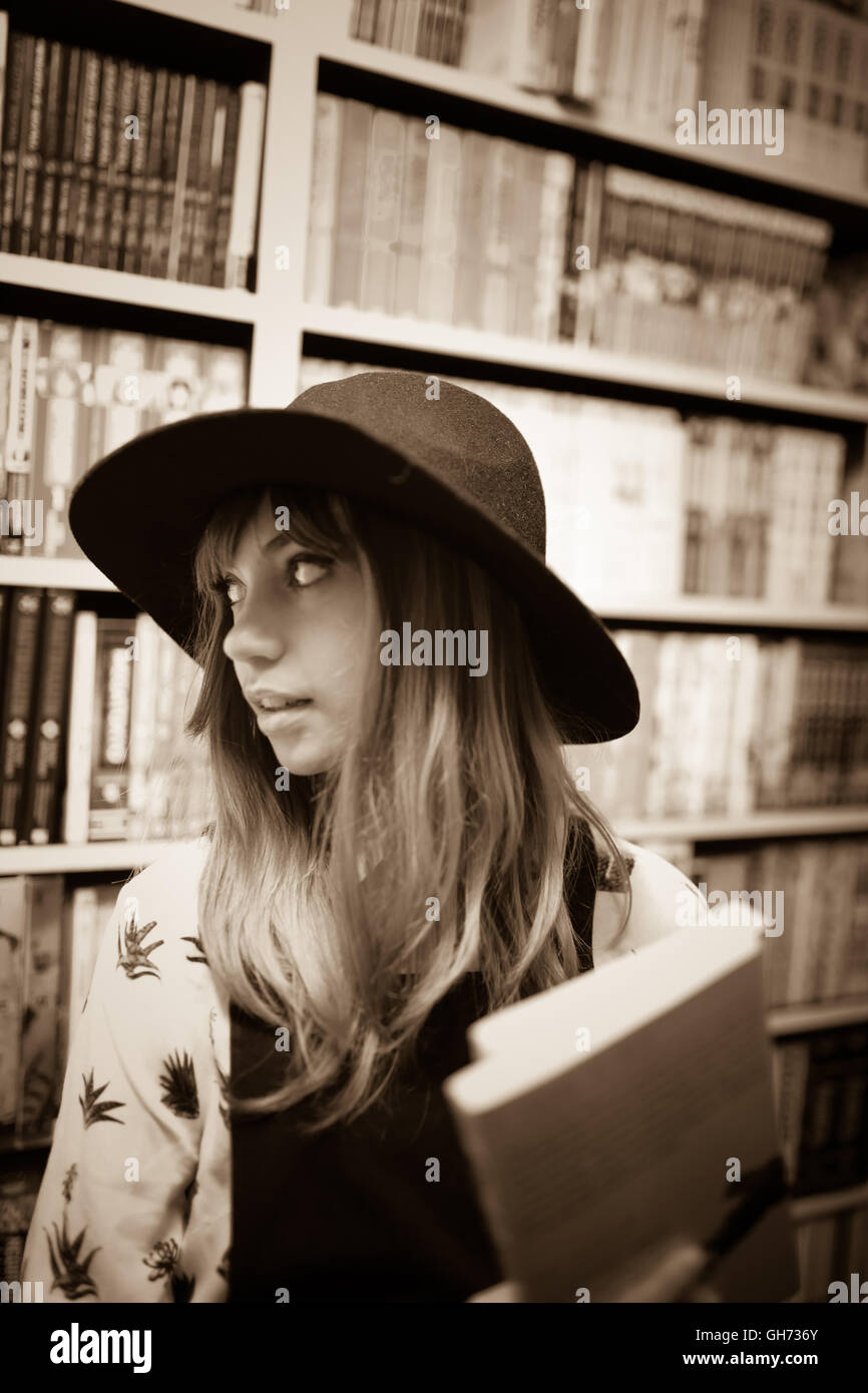 Seppia fotografia di un dodicenne bionda ragazza caucasica indossando un cappello nero in un comic book store azienda 2 Manga libri, Foto Stock
